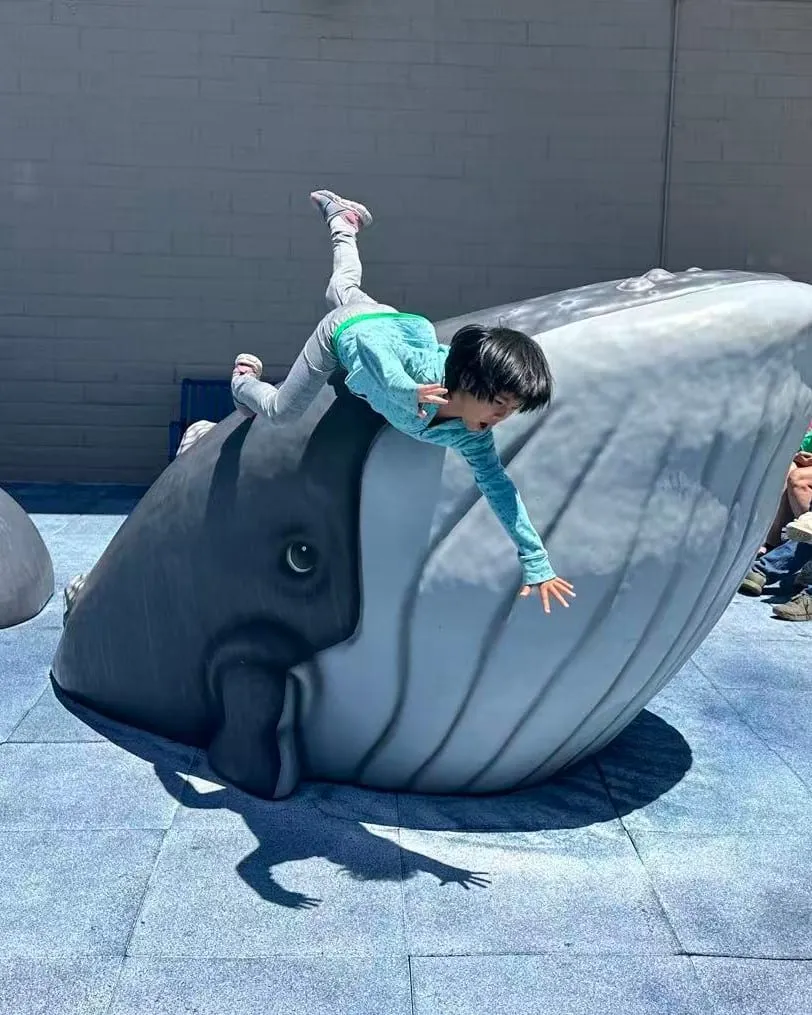 A young child climbing on a large whale sculpture in a courtyard