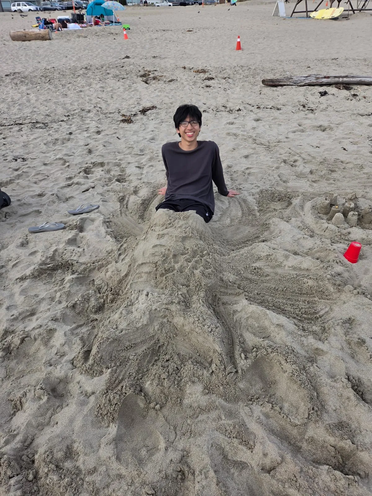 Ian sitting inside a large sand sculpture on a beach