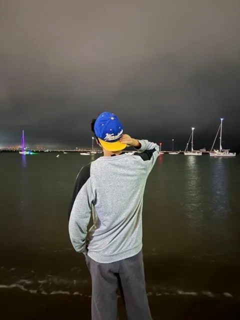 Ian in a baseball cap looking out at boats on the water at night